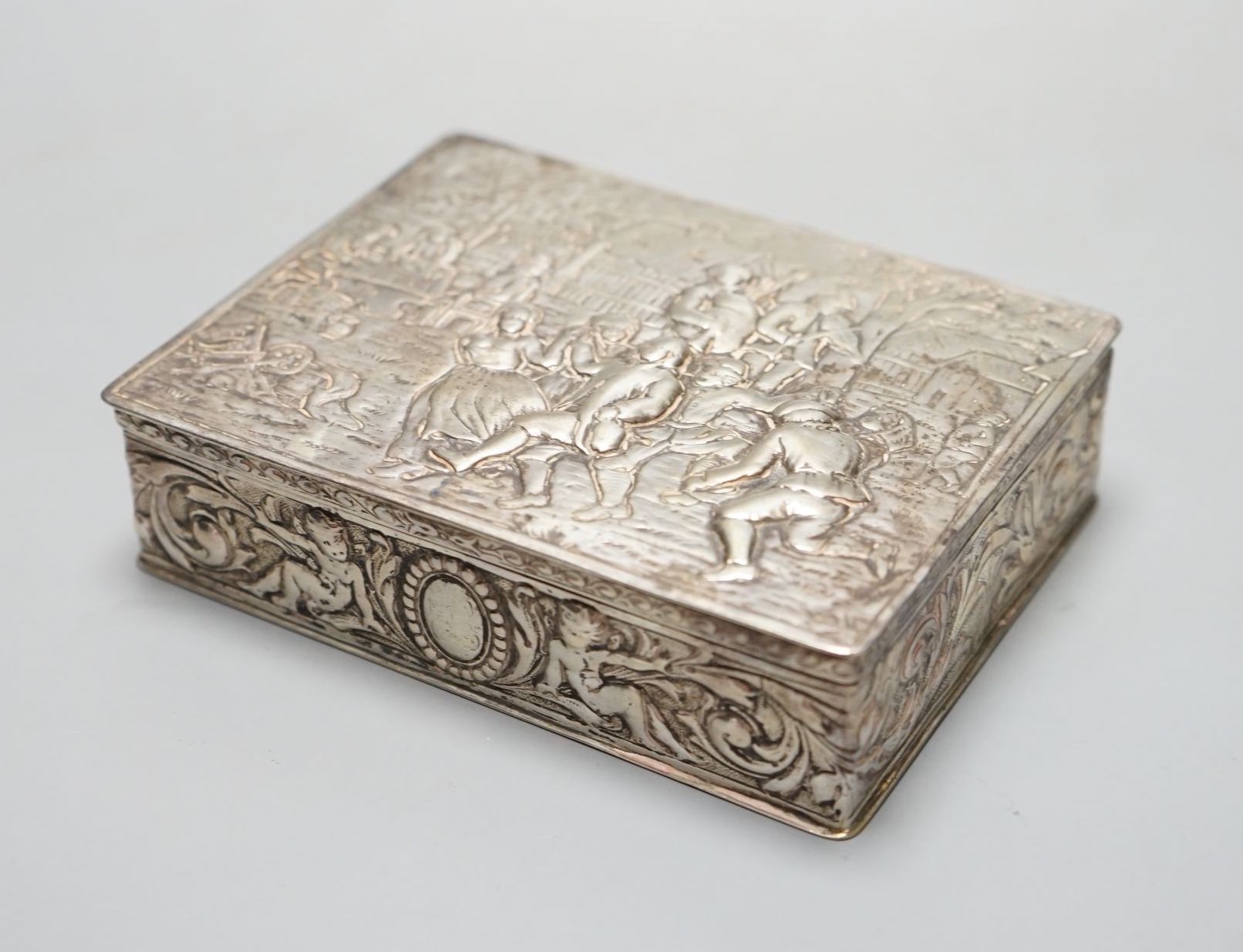 A late 19th / early 20th century German Hanau silver rectangular box and cover, the top embossed with a scene of revellers, import marks for London, 1912, 11.7cm.